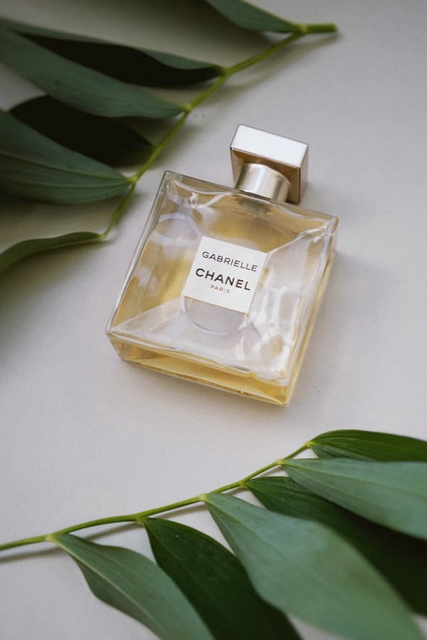 Gabrielle Chanel perfume bottle on a pale surface with green leaves around it, label reads Gabrielle Chanel Paris, elegant and luxurious mood